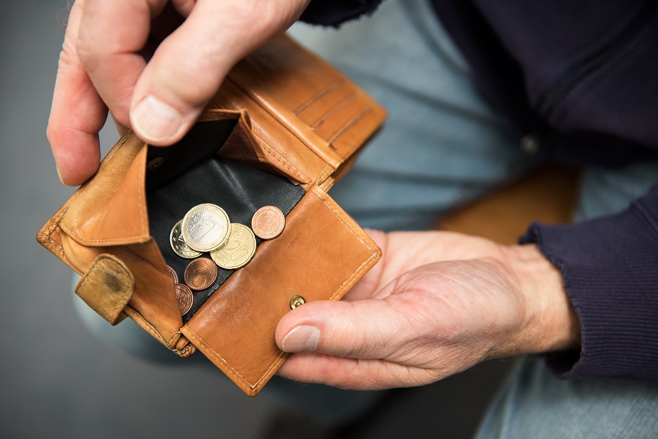 Wenig Geld zur Verfügung Hände eines Mannes halten eine Geldbörse offen, darin befinden sich wenige Münzen.