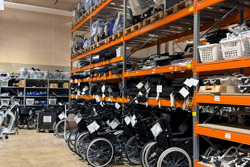 Lager für Pflege-Hilfsmittel in Apenrade Das Hilfsmittellager im dänischen Apenrade mit großen Regalen, in denen zahlreichen Pflegehilfsmittel gelagert sind, unter anderem stehen dort Rollstühle aufgereiht.