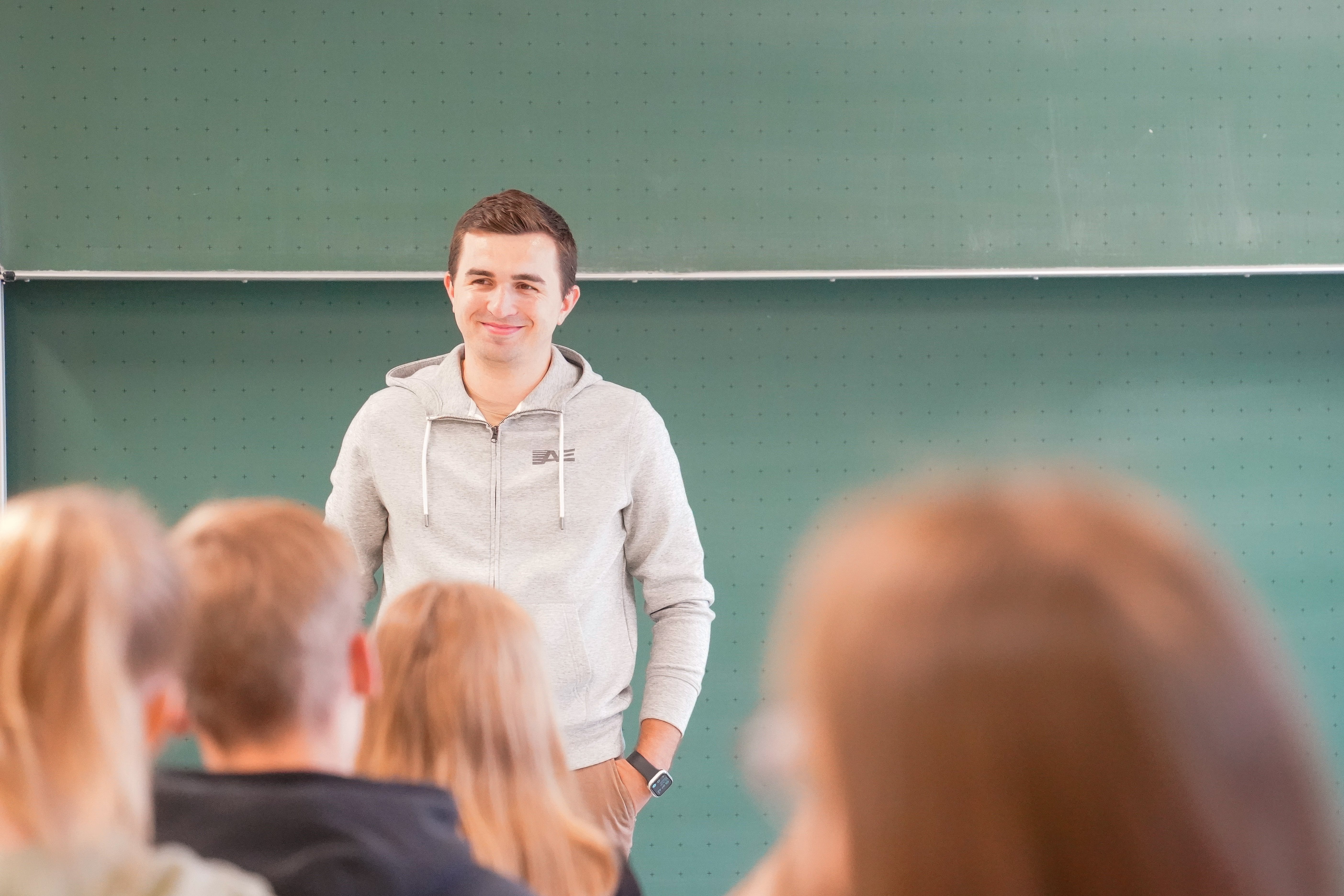 Ricardo Scheuerer Barrierefreiheit Ricardo Scheuerer steht vor einer grünen Tafel, blickt lächelnd in eine Gruppe von Zuhörenden bei einem Vortrag an der Uni Paderborn.