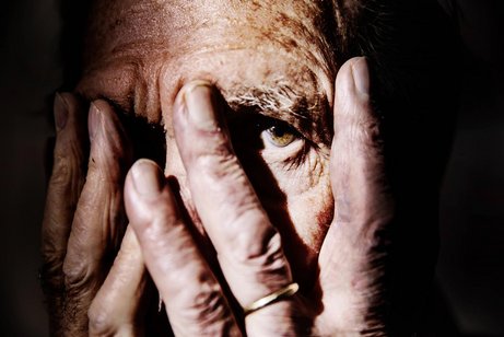 Älterer Mensch hält sich die Hände vor die Augen und schaut verängstigt zwischen den Fingern hindurch