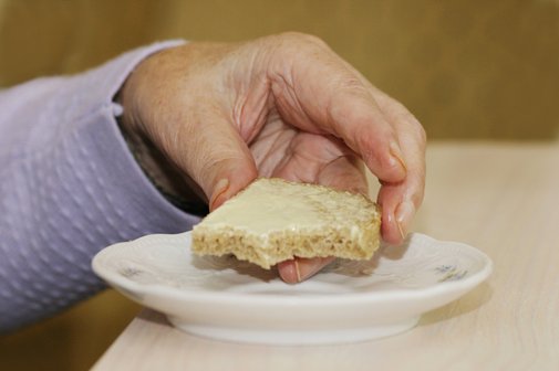 Essen in einem Altersheim Die Hand einer Frau in einem Altersheim greift nach einem Buttebrot