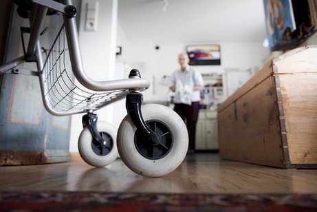 Blick in eine Küche, man sieht die Räder eines Rollators im Vordergrund, im Hintergrund verschwommen ein älterer Mann.