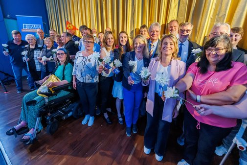 Gruppenbild: Ehrenamtlich Engagierte des VdK stehen in einer großen Gruppe vor der Leinwand im Kinosaal, der goldene Vorhang ist geschlossen.