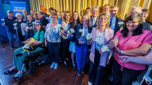 Gruppenbild: Ehrenamtlich Engagierte des VdK stehen in einer großen Gruppe vor der Leinwand im Kinosaal, der goldene Vorhang ist geschlossen.
