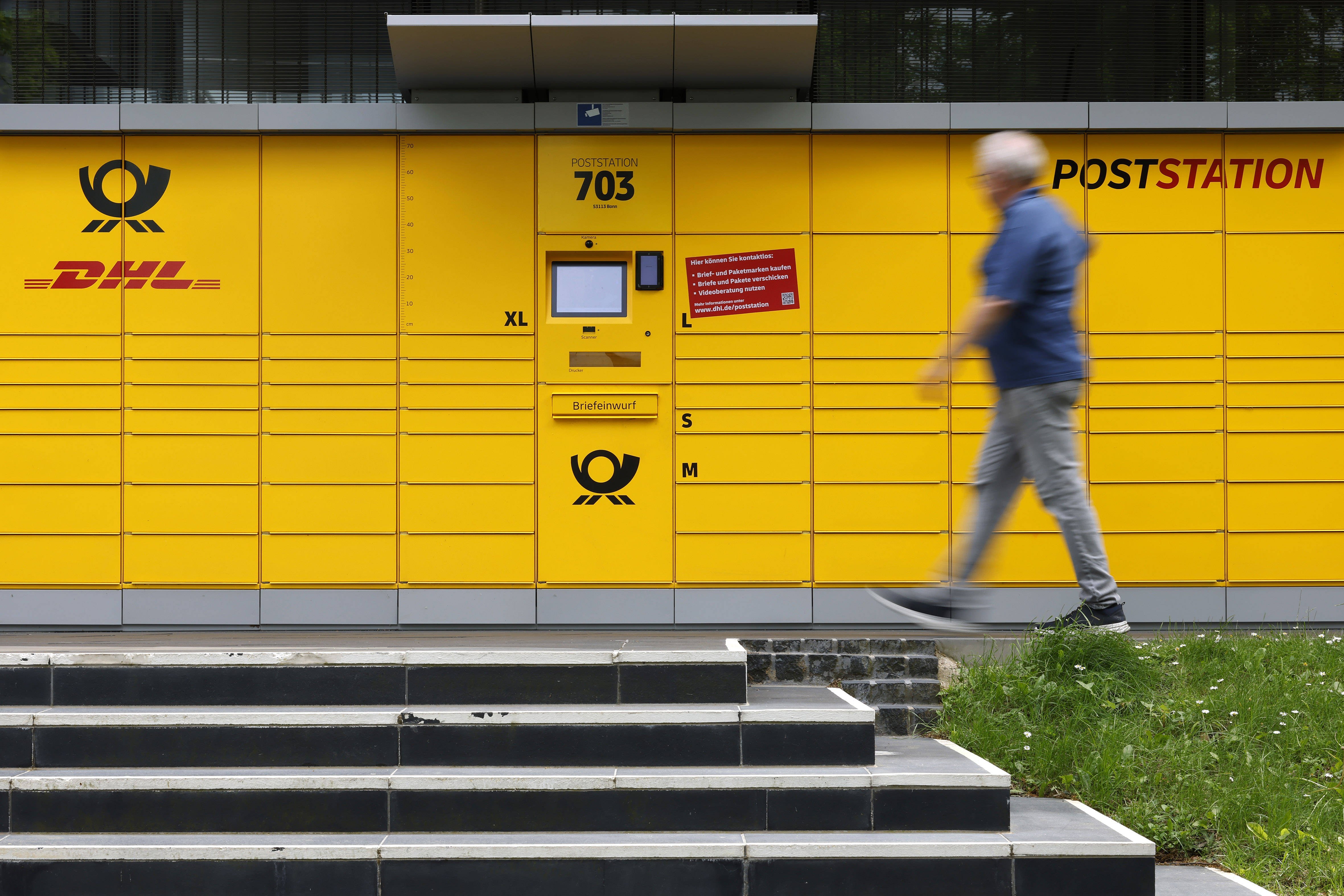 Eine Poststation von DHL. Ein Mann geht gerade daran vorbei. Im Vordergrund sieht man eine Treppe.