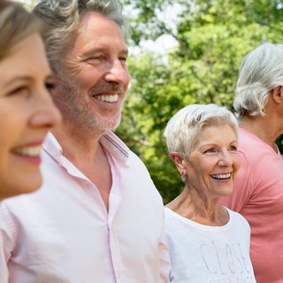 Mehrere Männer und Frauen sind gut gelaunt, lachen. Sie sind draußen im Grünen. 