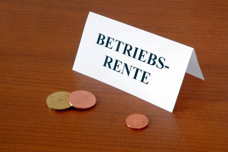 Betriebsrente Ein Schild mit der Aufschrift "Betriebsrente" steht auf einem Tisch, davor liegen Centmünzen