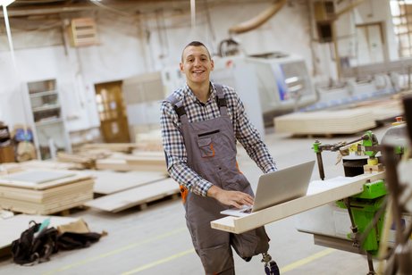 Ein junger Mann mit einer Beinprothese an seinem Arbeitsplatz in einer M&ouml;belfabrik.