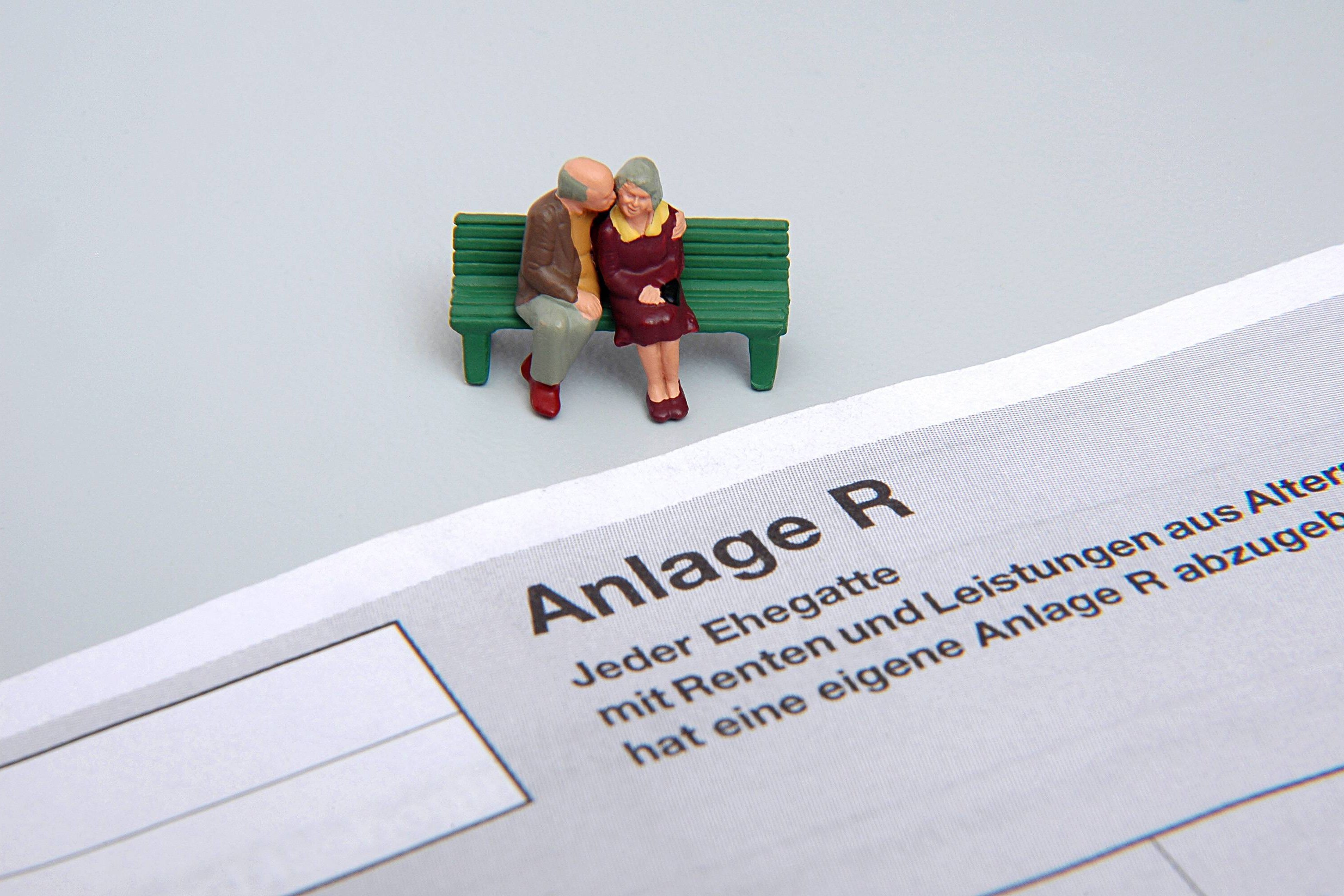 Anlage R bei der Steuererklärung Steuererklärung der Renteneinkünfte: Figuren eines Rentnerehepaares sitzen auf einer Bank vor dem Formular - Anlage R -
