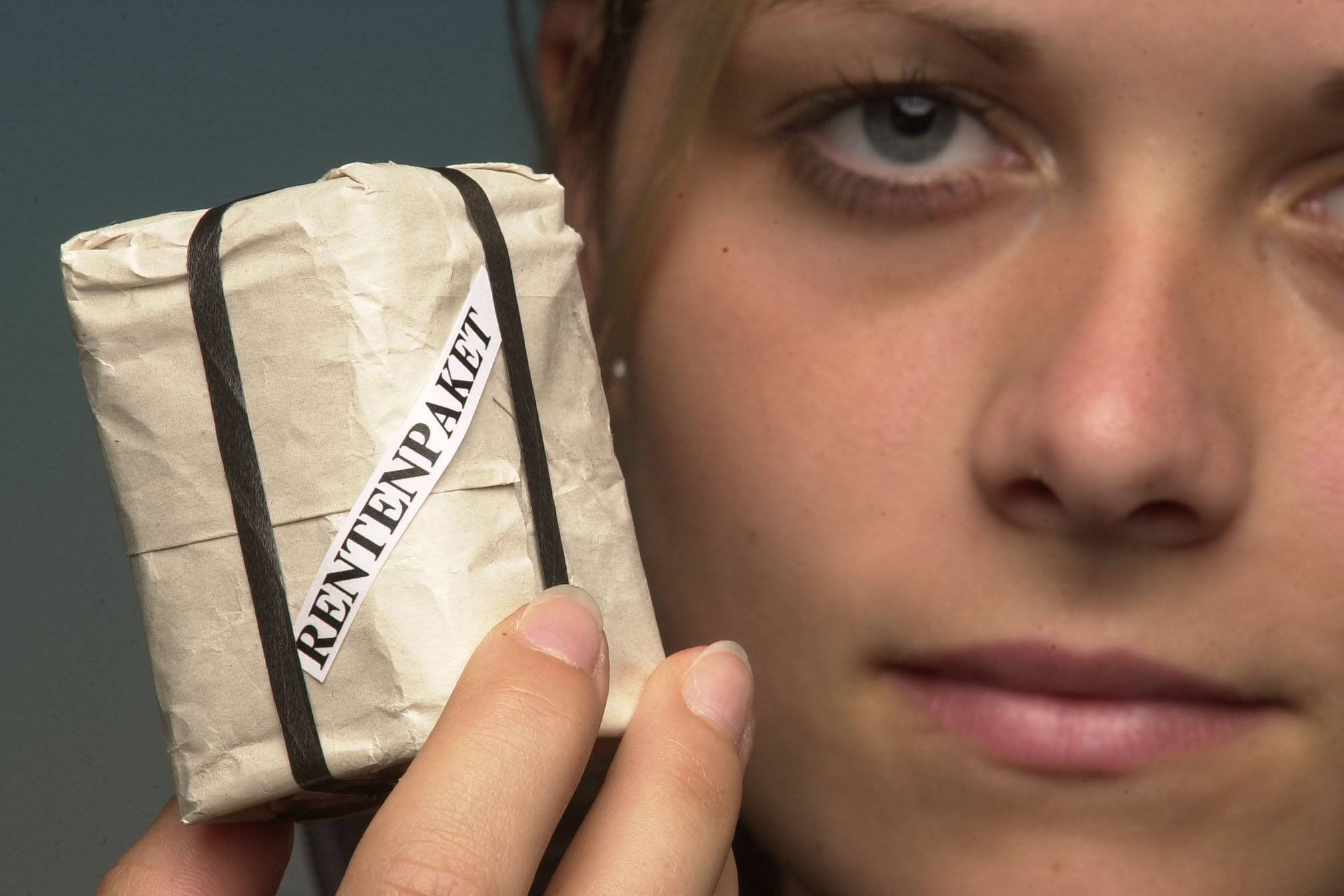 Rentenpaket Eine junge Frau hält ein kleines Päckchen in der Hand, auf der Verpackung steht "Rentenpaket". Ihr Gesichtsausdruck ist skeptisch.