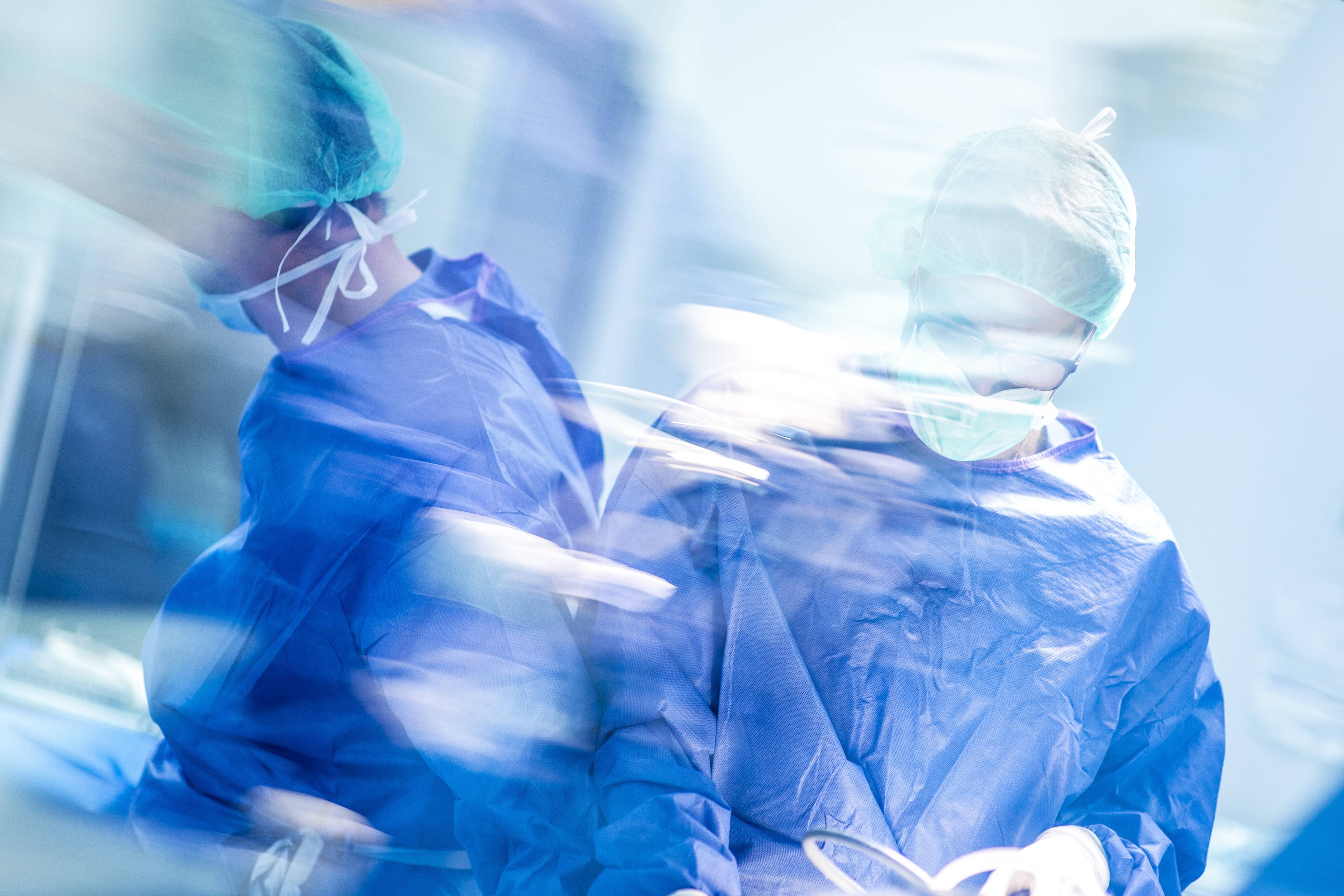 Operation im Krankenhaus Verschwommene Aufnahme zweier männlicher Chirurgen während einer Operation, sie tragen blaue OP-Kleidung