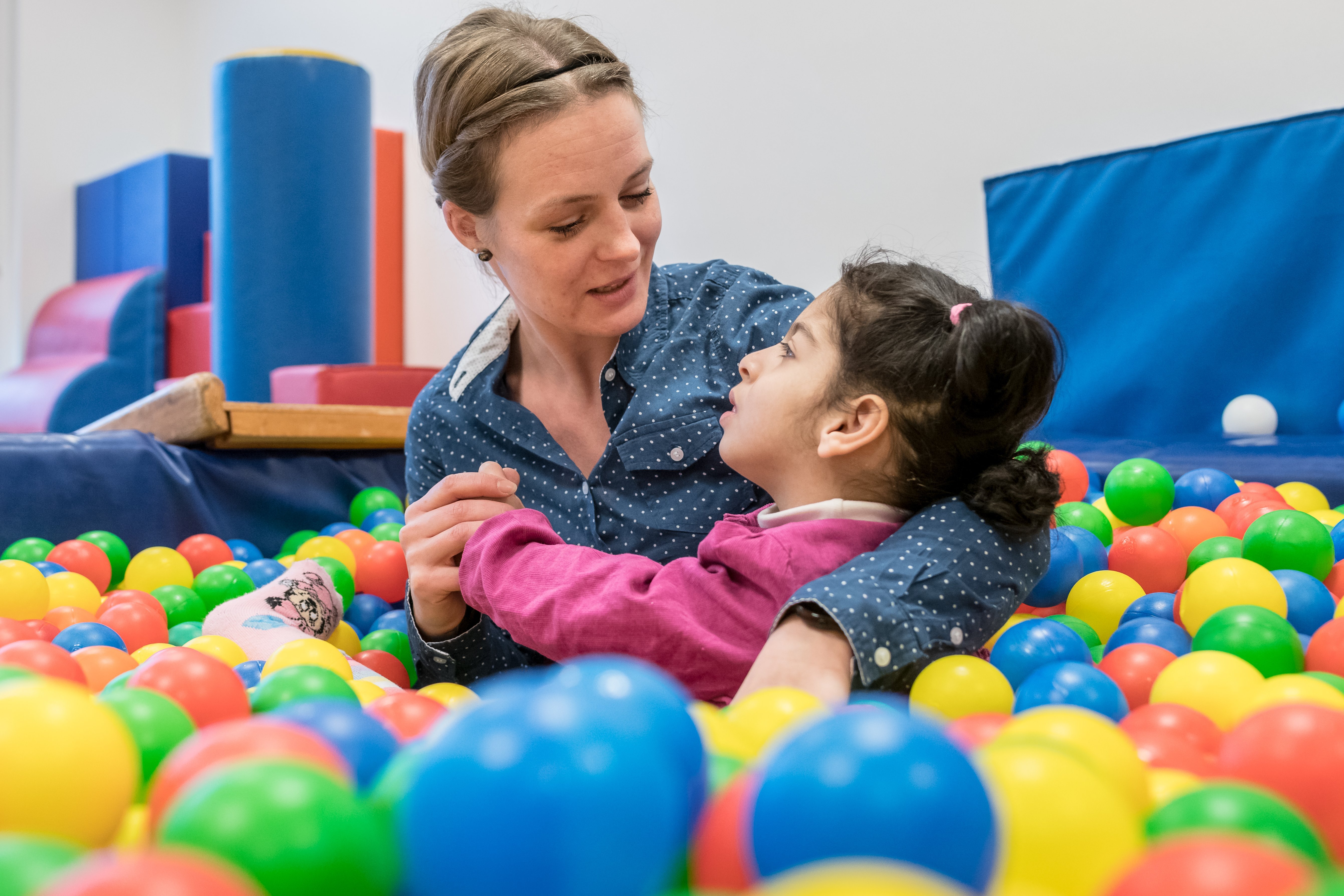 Assistenz für Kinder mit Behinderung Das Foto zeigt eine junge Inklusionshelferin beim Spiel im Bällebad mit der einem schwerst mehrfach behinderten Mädchen