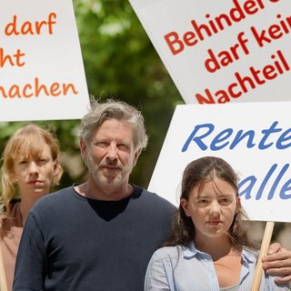 Gruppe von Menschen verschiedenen Geschlechts und Alters, mit und ohne Behinderung, demonstrieren. Auf den Demopappen steht "Pflege darf nicht arm machen", "Behinderung darf kein Nachteil sein" und "Rente für alle"