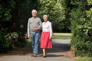 Ein älterer Mann und eine ältere Frau gehen gemeinsam spazieren im Park, sie halten sich an der Hand