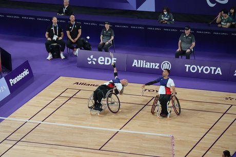 homas Wandschneider (links) und Rick Cornell Hellmann beim Rollstuhl-Badminton. Der linke streckt sich aus seinem Rollstuhl weit nach oben, um den Ball zu schlagen.