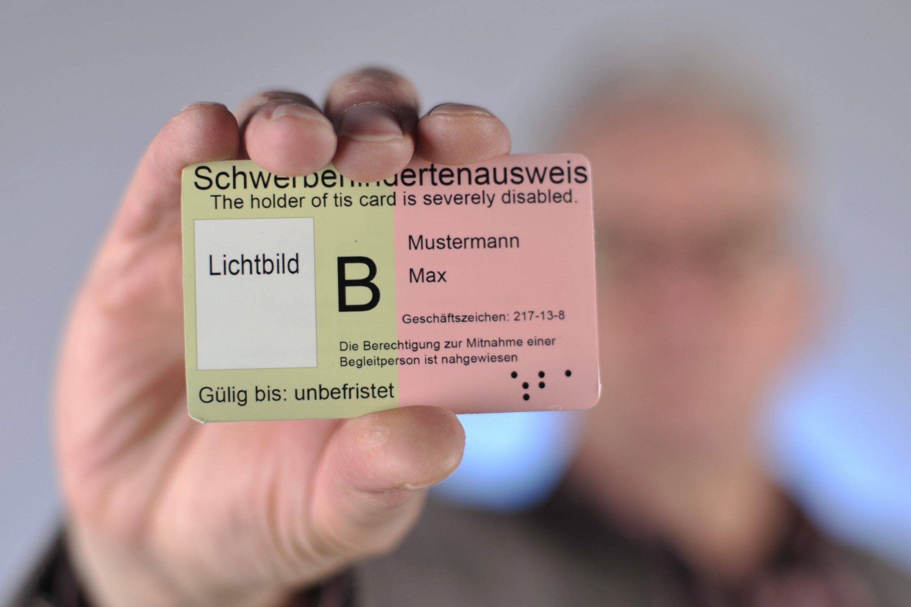 Schwerbehindertenausweis Ein Mann hält einen Schwerbehindertenausweis mit dem Merkzeichen B in die Kamera.