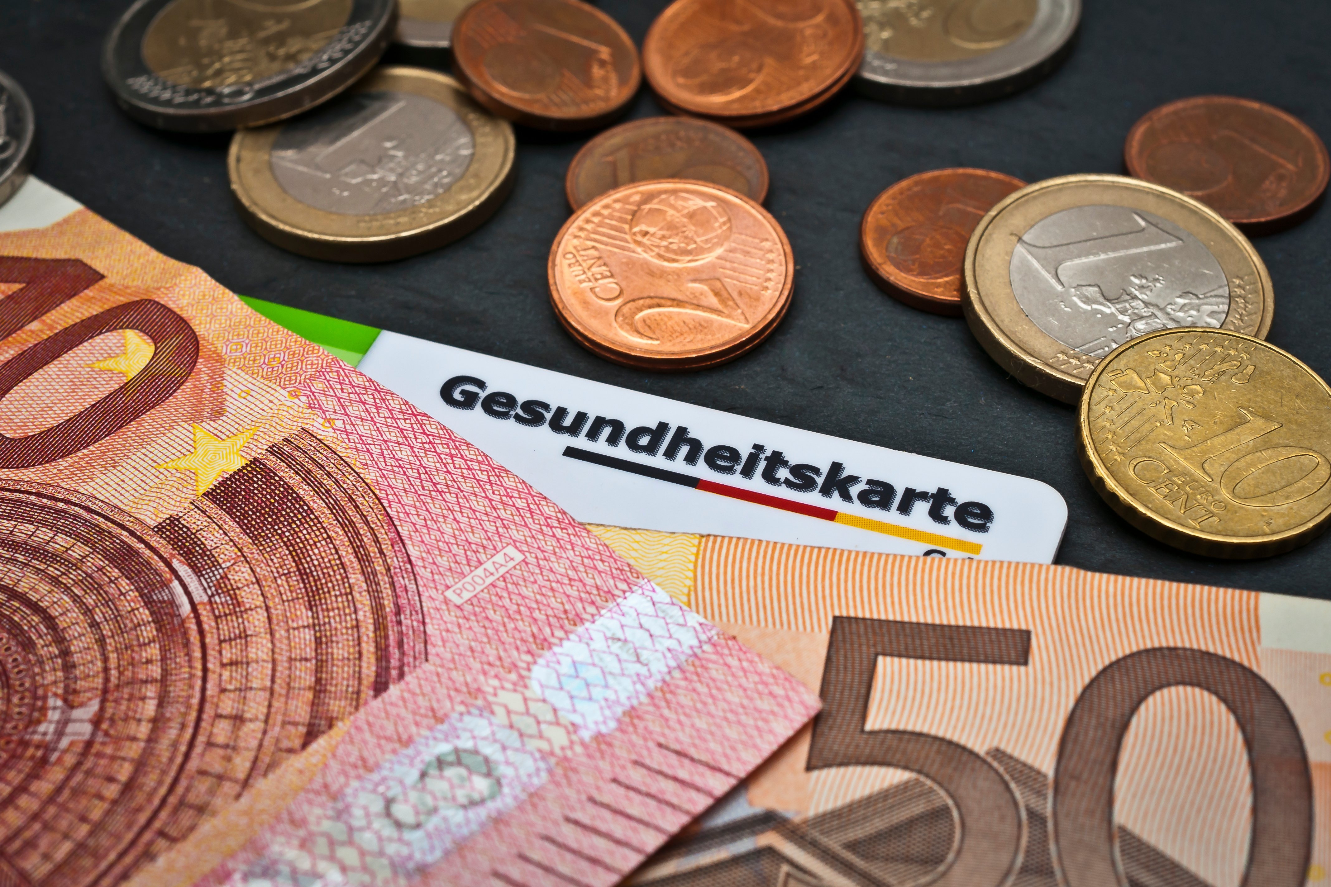 Geldscheine und M&uuml;nzen, darunter liegt eine Gesundheitskarte.