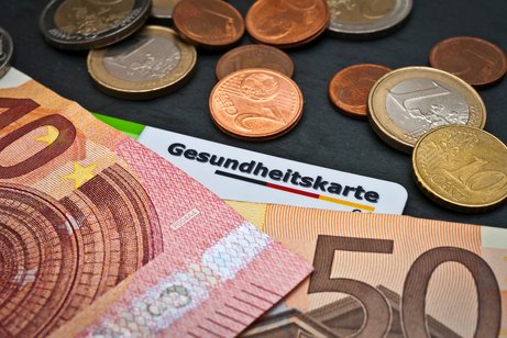 Gesundheitssystem Kosten Geldscheine und Münzen, darunter liegt eine Gesundheitskarte.