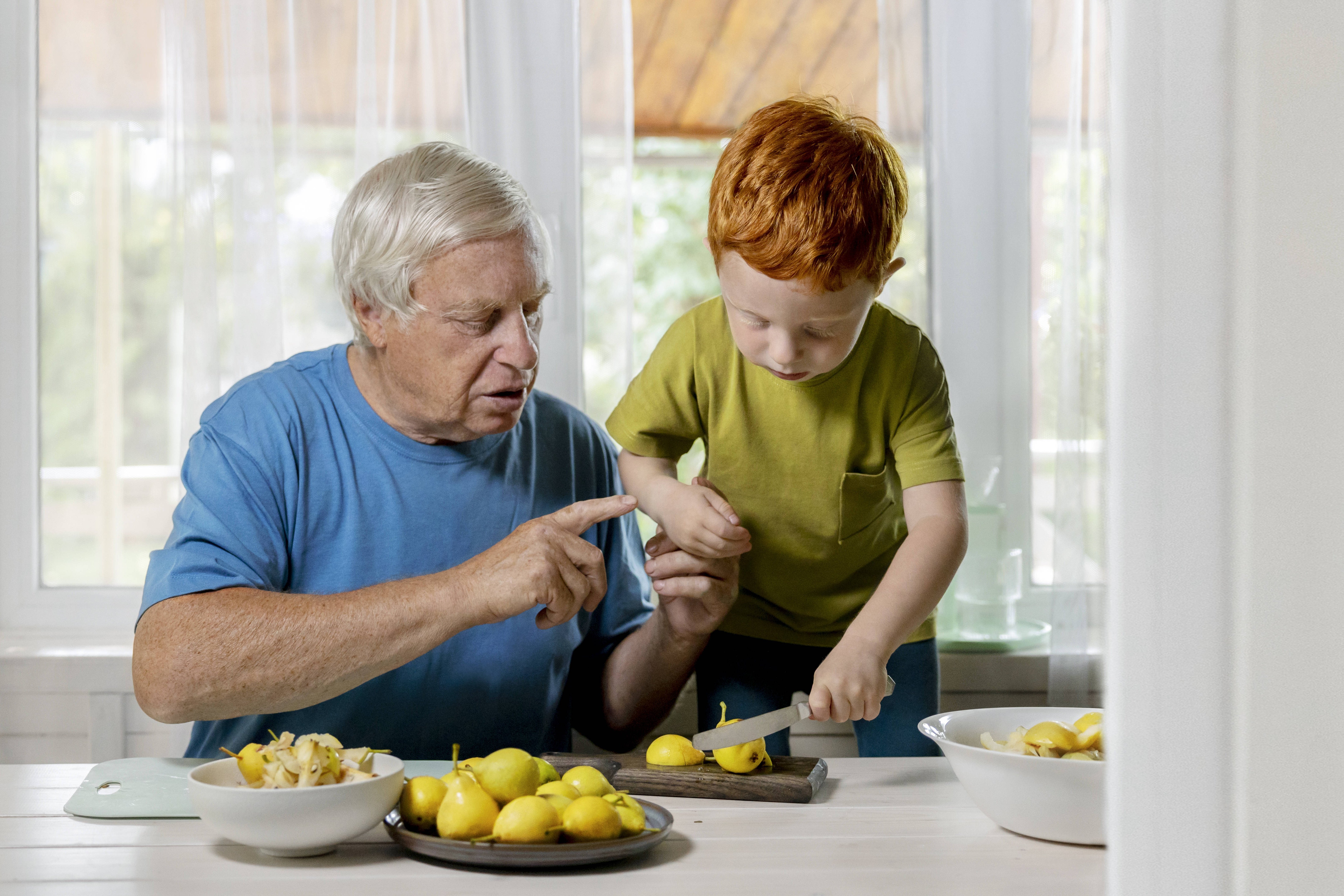 Gesunde Ernährung im Alter Ein älterer Mann sitzt am Tisch und schneidet Zitronen auf, ein Kind - vermutlich sein Enkel - schaut interessiert zu.
