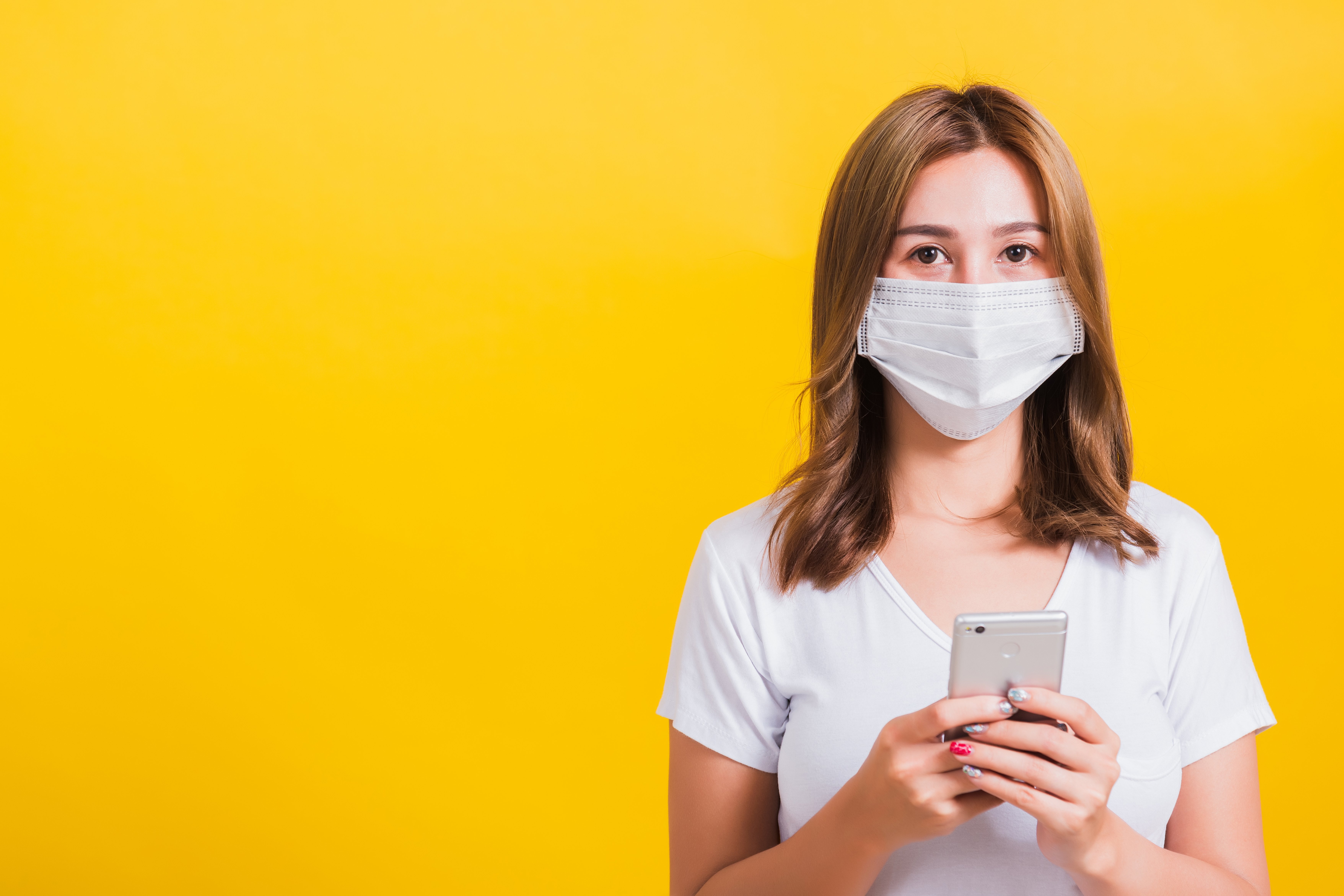 Digitale Gesundheitsanwendungen Eine junge Frau, die einen Mundschutz trägt, hält ein Smartphone in der Hand.