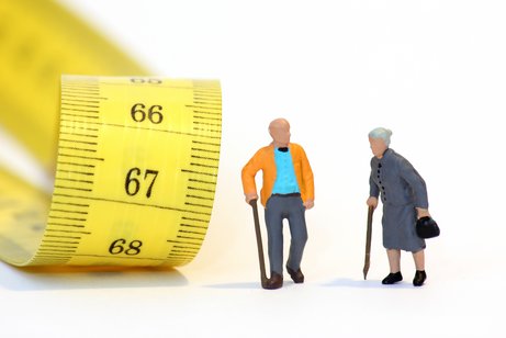 Rentenalter Zwei Rentner-Figürchen - ein Mann und eine Frau - vor einem gelben Maßband, auf dem die Zahlen 66, 67 und 68 zu sehen sind.