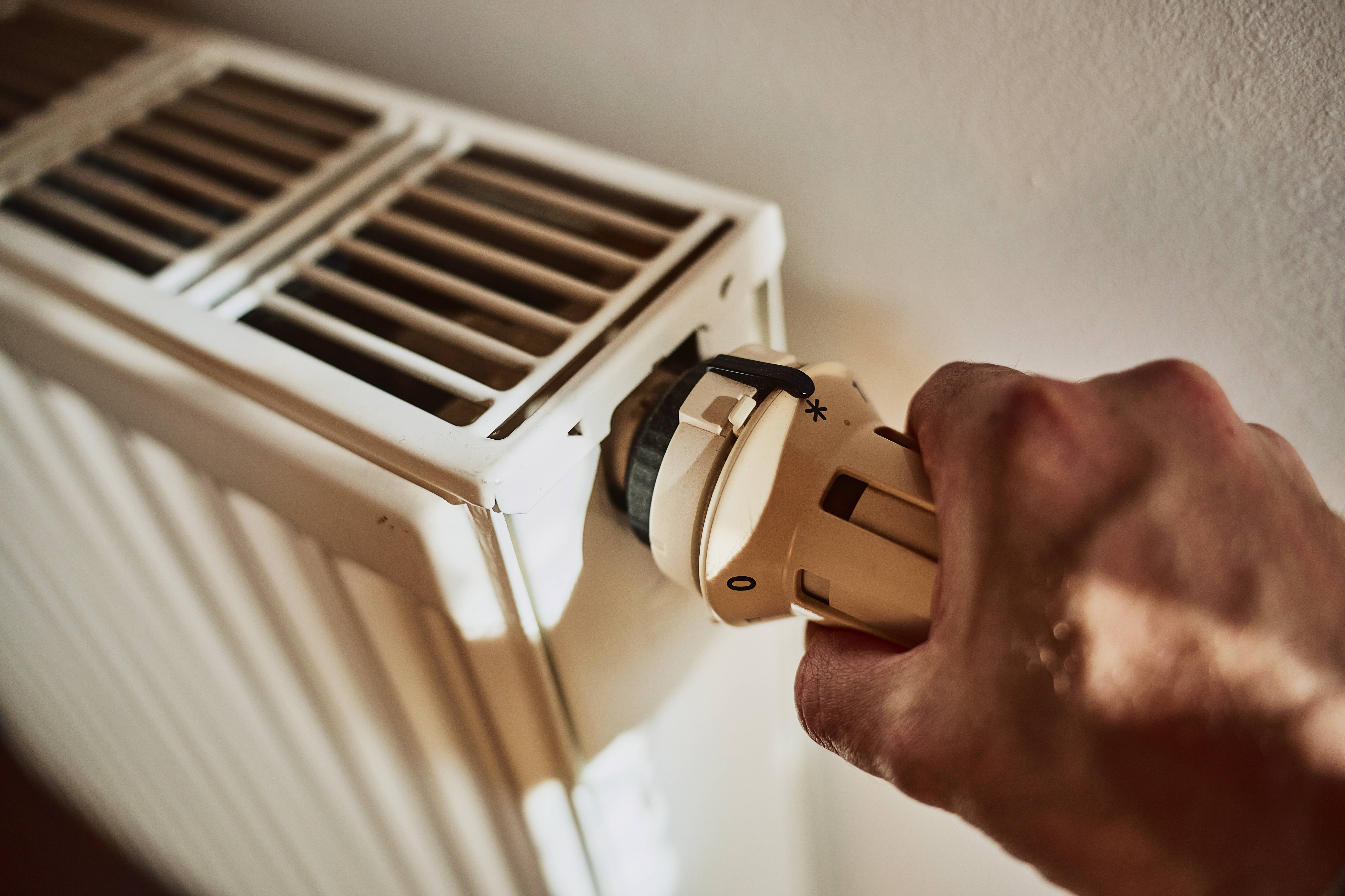 Heizkosten Die Hand von einem Mann dreht am Thermostat von einem Heizkörper.