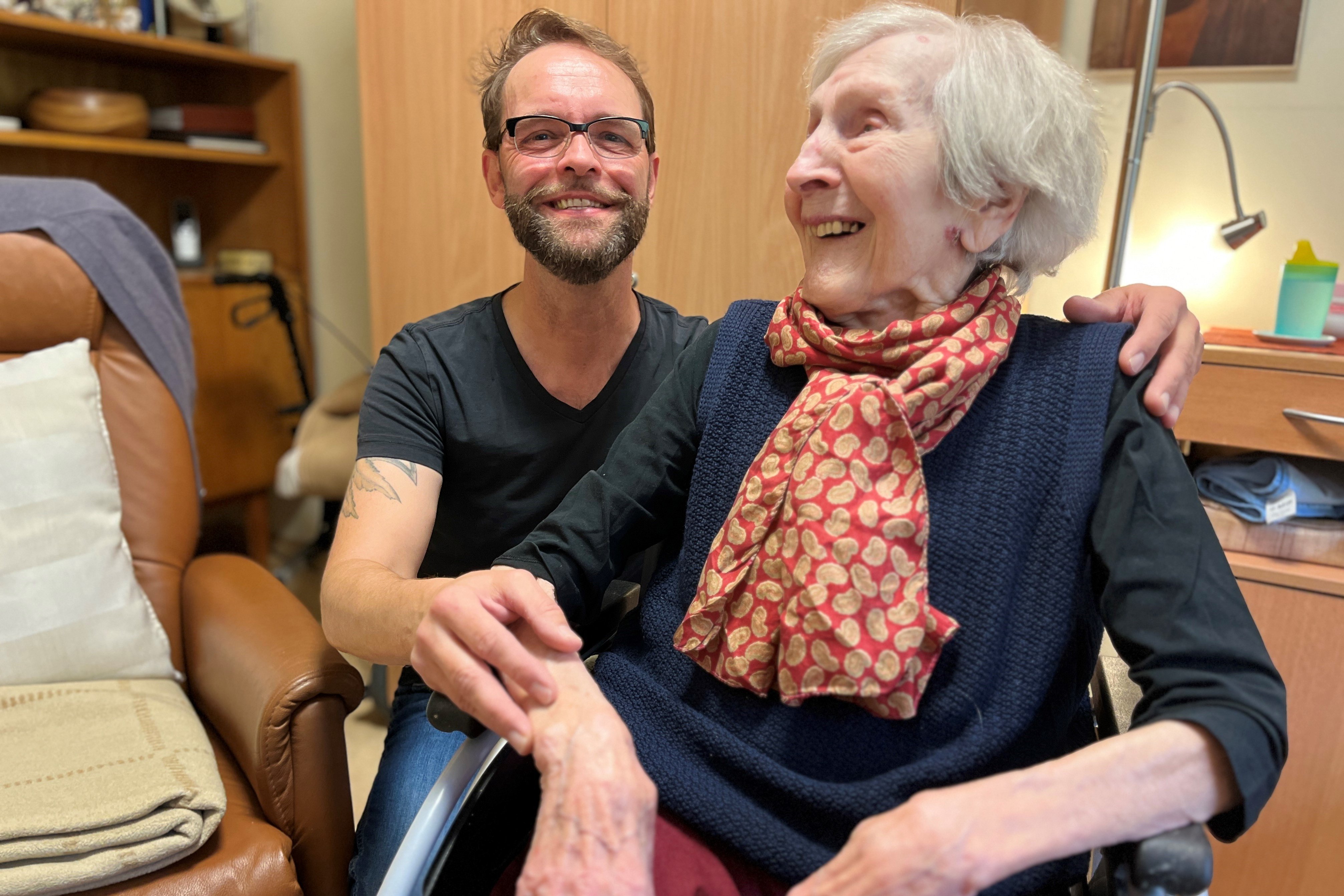Besuch im Seniorenheim Dirk Angele und Anita Göbels, die Bewohnerin des Seniorenheims, in dem Dirk Angele ehrenamtlich tätig ist. Sie sitzt im Rollstuhl, er sitzt hinter ihr, legt eine Hand auf ihre Schulter und die andere auf ihren Arm.