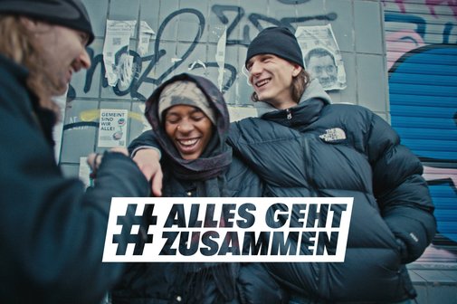 Alles geht zusammen - Jugendliche Drei Jugendliche stehen vor einer mit Graffiti besprühten Wand, sie lachen zusammen, einer hat den Arm über die Schulter des anderen gelegt. Darüber das Logo der Aktion Alles geht zusammen.