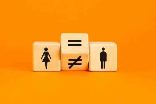 Drei W&uuml;rfel liegen nebeneinander vor orangenem Hintergrund. Einer zeigt ein Piktogramm einer Frau, einer das eines Mannes. Dazwischen liegt ein gekippter W&uuml;rfel auf der Kante, der ein Gleichheits- und ein Ungleichheitszeichen anzeigt.