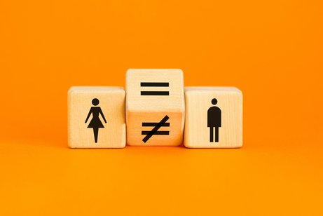 Drei W&uuml;rfel liegen nebeneinander vor orangenem Hintergrund. Einer zeigt ein Piktogramm einer Frau, einer das eines Mannes. Dazwischen liegt ein gekippter W&uuml;rfel auf der Kante, der ein Gleichheits- und ein Ungleichheitszeichen anzeigt.