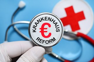 Die Bildmontage zeigt eine Hand mit medizinischem Handschuh, die eine Stethoskop hält, in dessen Mitte das Wort "Krankenhausreform" und ein Euro-Zeichen stehen. 
