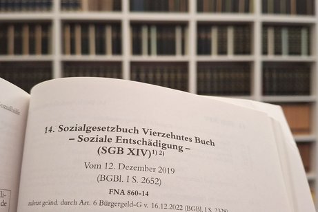 Ein aufgeschlagenes SGB 14, im Hintergrund sieht man Regale mit Fachbüchern.