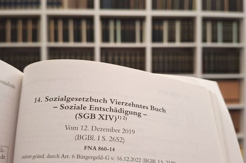 Ein aufgeschlagenes SGB 14, im Hintergrund sieht man Regale mit Fachbüchern.