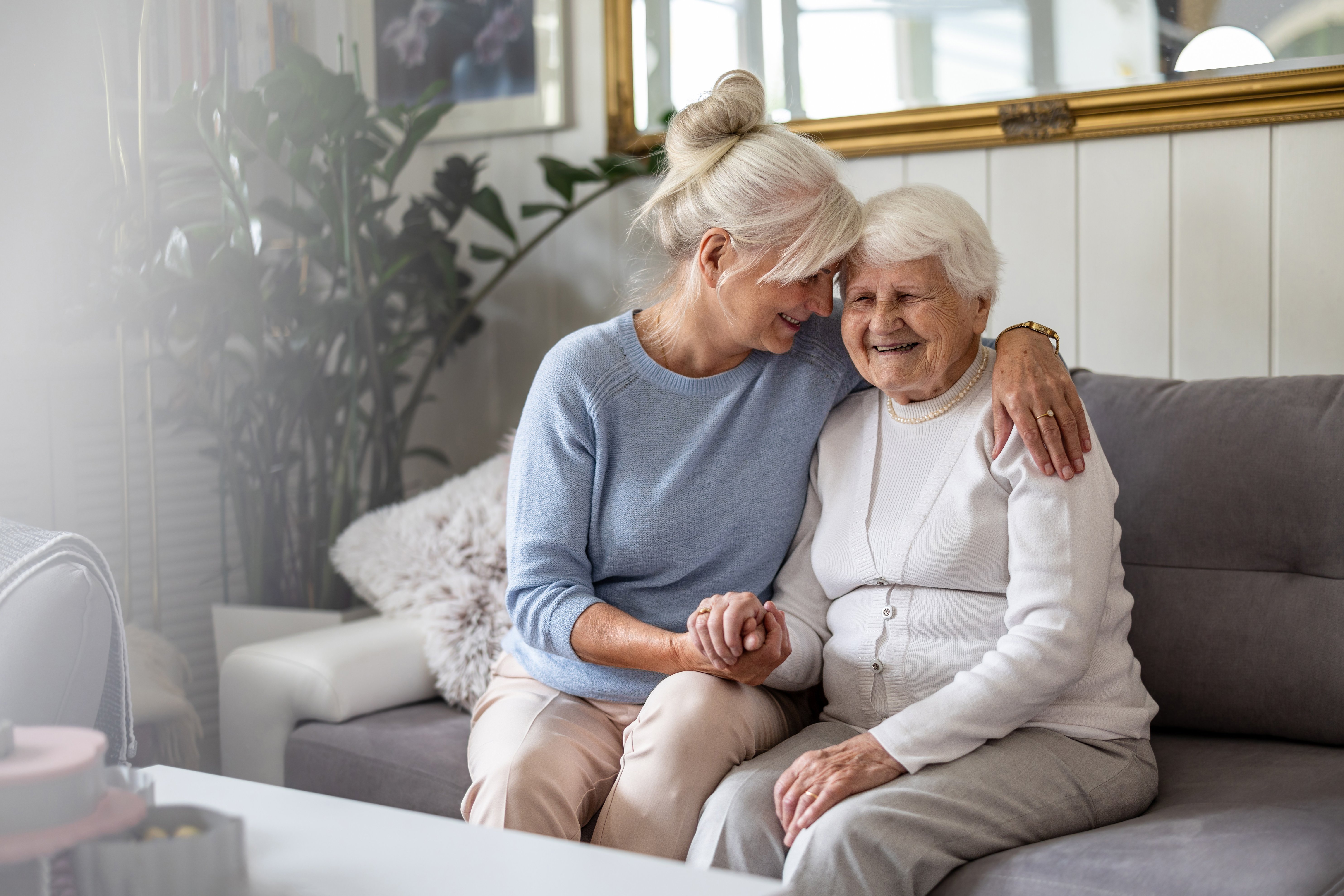 Eine &auml;ltere Frau sitzt mit einer noch &auml;lteren Seniorin auf einem Sofa, sie nimmt die &Auml;ltere liebevoll in dem Arm. Das Bild strahlt N&auml;he und Liebe aus. 
