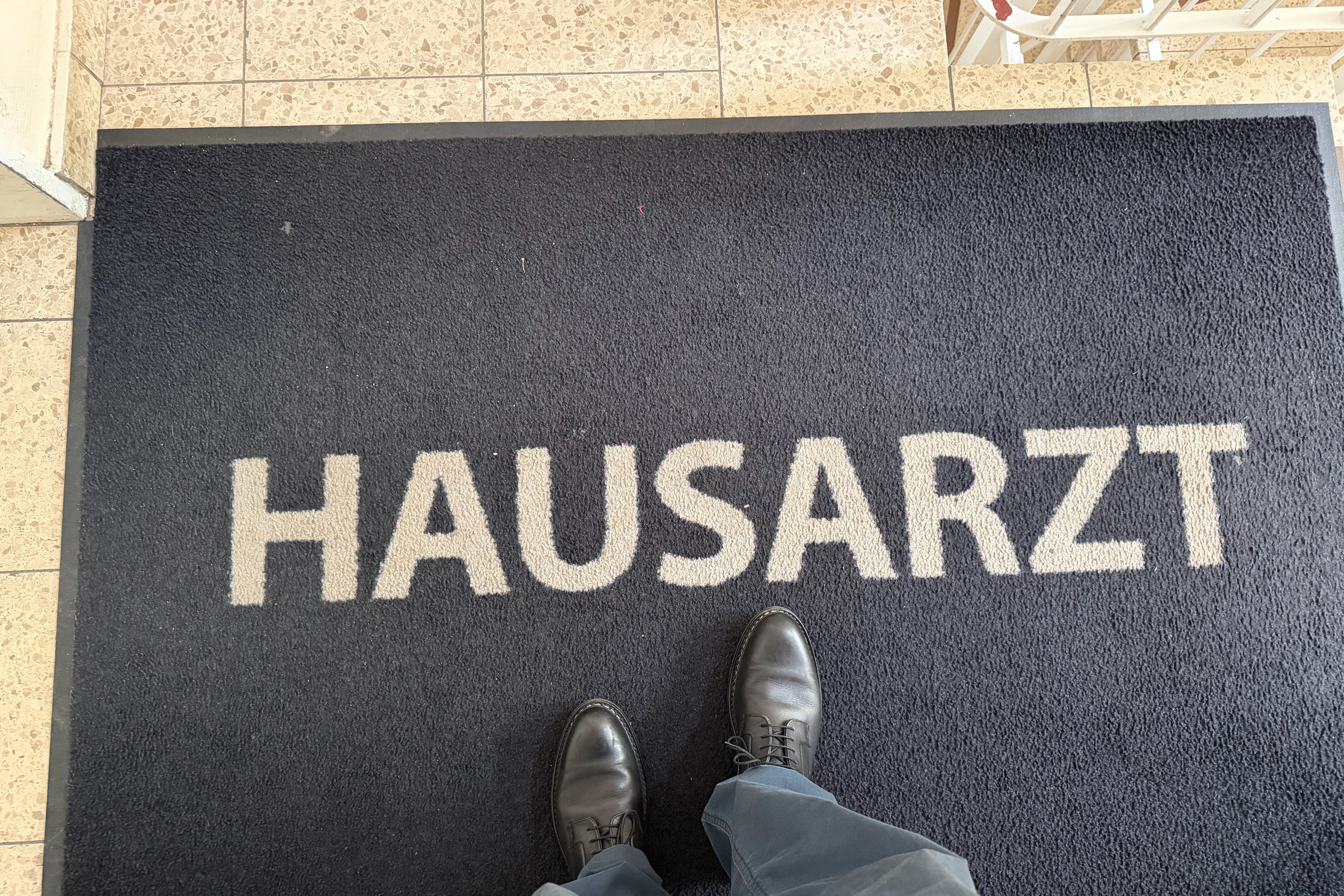 Jemand steht auf einer Fu&szlig;matte, auf der "Hausarzt" in Blockbuchstaben geschrieben steht