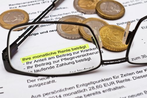 Nahaufnahme eines Rentenbescheids mit markiertem Text ‚Ihre monatliche Rente beträgt‘, umgeben von Euro-Münzen und einer Brille im Vordergrund.