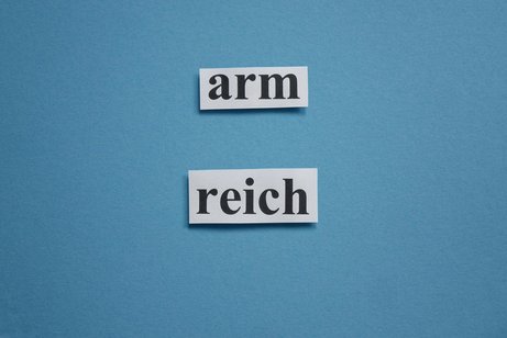 Ungleiche Vermögensverteilung Auf blauem Grund stehen die Wörter "arm" und "reich" aus ausgeschnittenem Papier