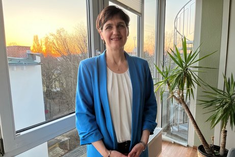 Katja Urbatsch am Fenster, neben ihr eine Zimmerpflanze