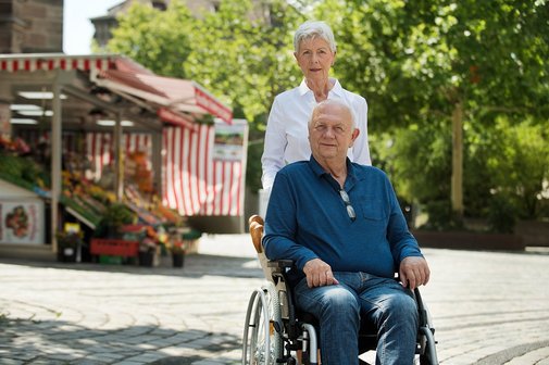 Paar geht spazieren Älteres Paar draußen unterwegs, er sitzt im Rollstuhl, sie schiebt ihn