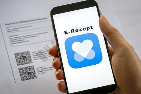  Eine Hand hält Smartphone. Darauf ist ein blaues Logo mit der Überschrift "E-Rezept". 