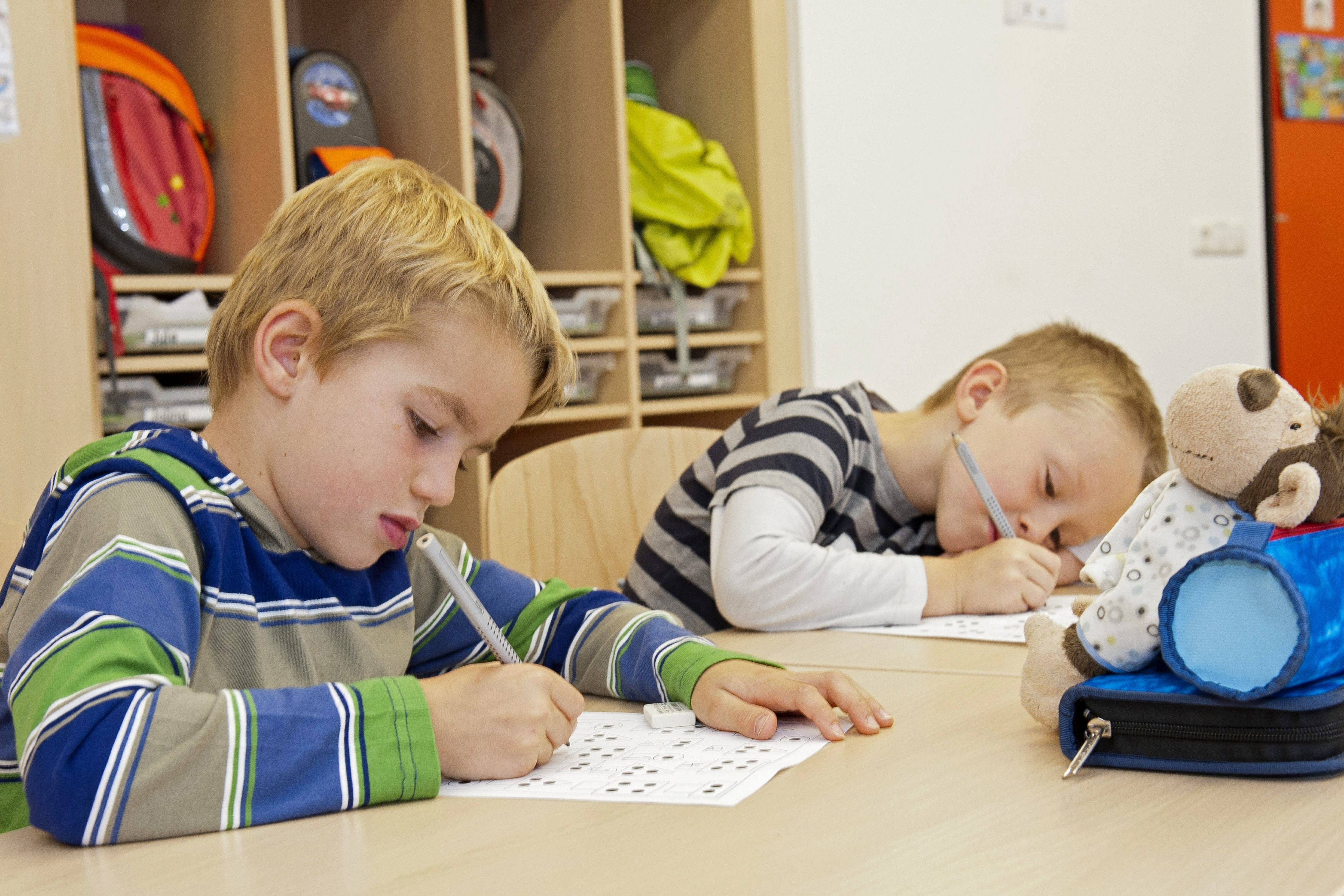 Zwei Erstklässler sitzen in einer Schule am Tisch, schreiben etwas auf ein Arbeitsblatt.