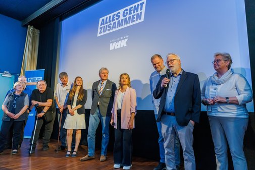 Mehrere ehrenamtlich Engagierte stehen mit VdK-Präsidentin Verena Bentele auf der Bühne, ein Mann spricht ins Mikrofon.