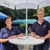 Conny Schuck und Gudrun Müller stehen nebeneinander an einem Info-Tisch des VdK Rheinland-Pfalz