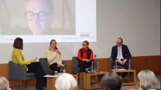 Blick auf das Podium bei der Veranstaltung. Zweite von links ist VdK-Präsidentin Verena Bentele, die gerade ins Mikrofon spricht. Per Zoom ist ein weitere Teilnehmer zugeschaltet, den man auf der Beamer-Leinwand sieht. 