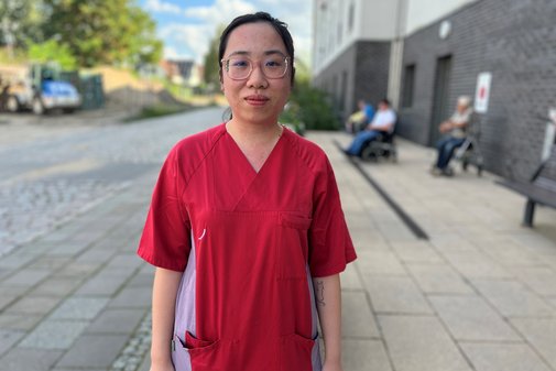 Pflegefachkraft Quynh Anh Das Foto zeigt Quynh Anh. Die junge Frau trägt einen roten Kasack.