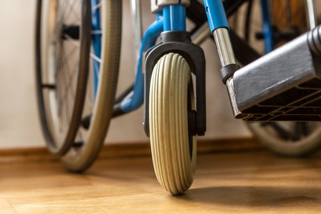 Nahaufnahme eines Rollstuhls: Man sieht ein gro&szlig;es und ein kleines Rad sowie einen Teil des Fu&szlig;teils