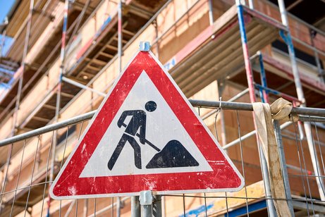 Wohnungsbau Ein Rohbau eine Gebäudes, davor ein großes Baustellen-Hinweisschild