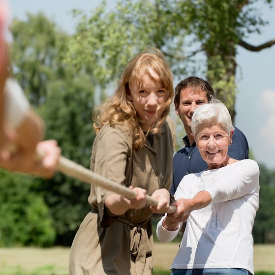 Tauziehen Ältere Frau, jüngere Fau und jüngerer Mann ziehen an einem Tau.