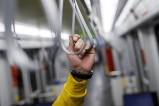 Eine Männerhand hält sich an einer Halteschlaufe in einer Straßenbahn fest. 