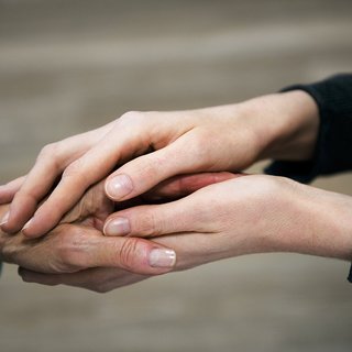 Die Hand einer jüngeren Frau hält die Hand einer älteren Frau in einer tröstenden Geste.